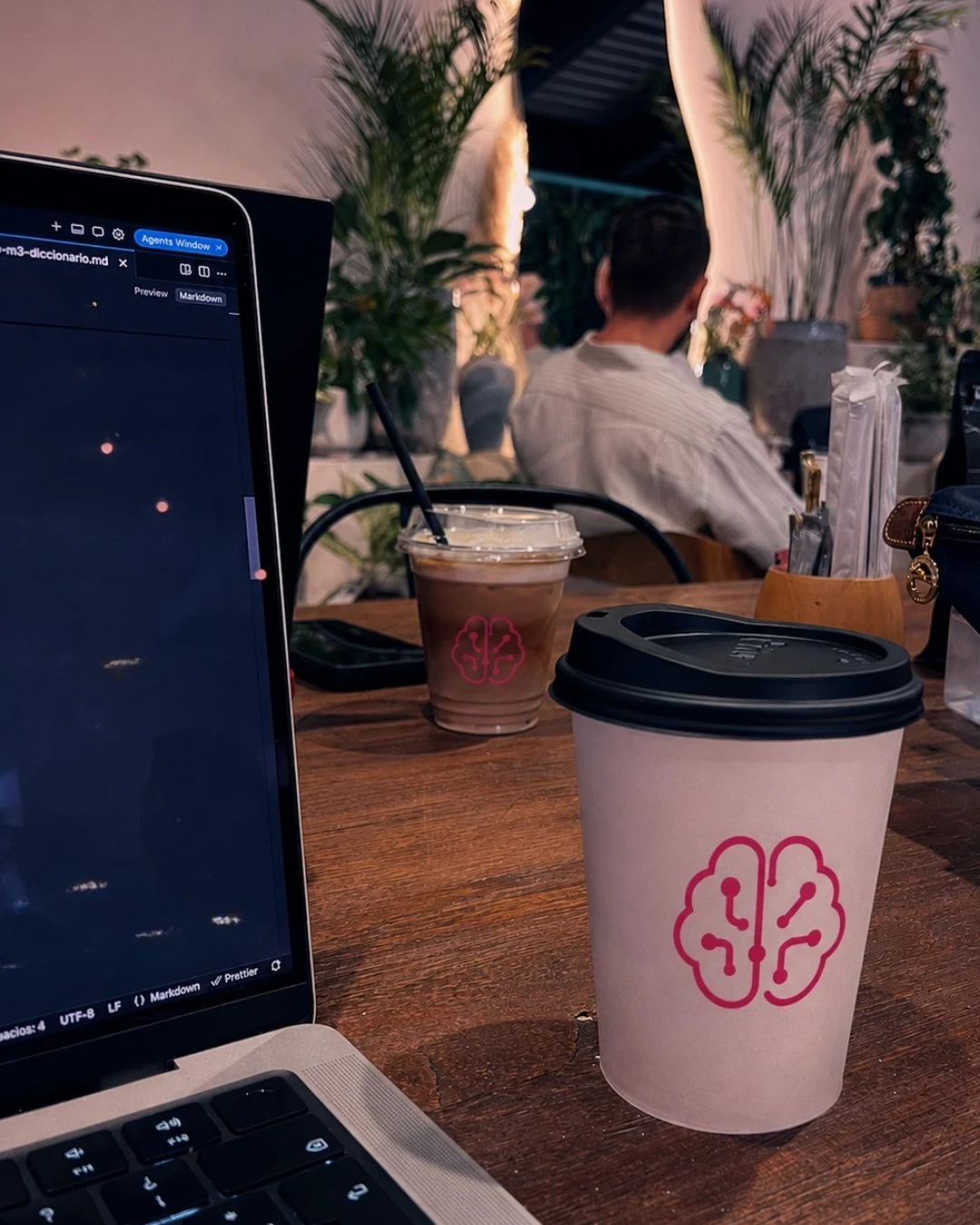 Un portátil con el editor abierto sobre una mesa de café, junto a dos vasos con el logotipo de aprenderIA en magenta