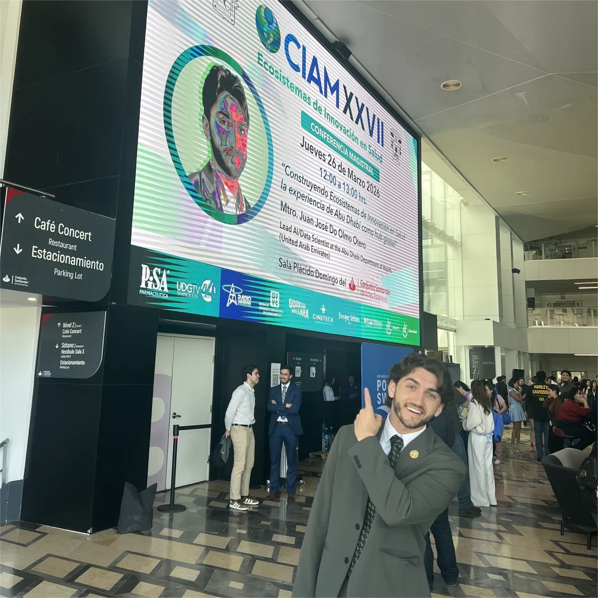 Un integrante del equipo señalando la pantalla del congreso CIAM XXVII, que anuncia su propia conferencia magistral