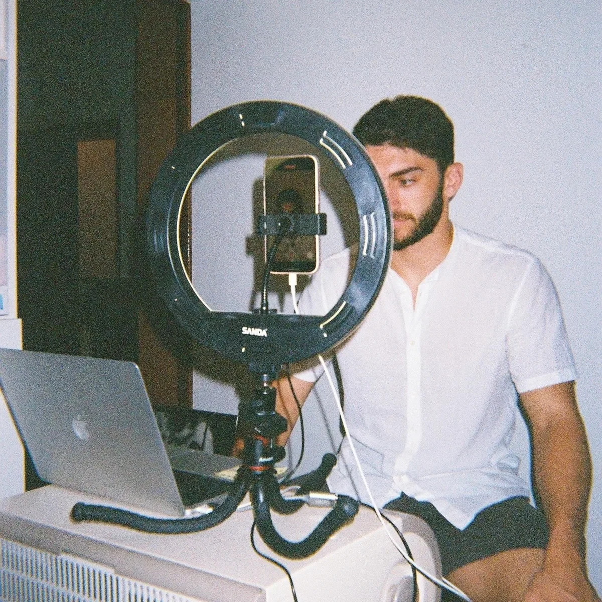 Un integrante del equipo grabando en casa con el móvil sujeto a un aro de luz, con el portátil abierto al lado
